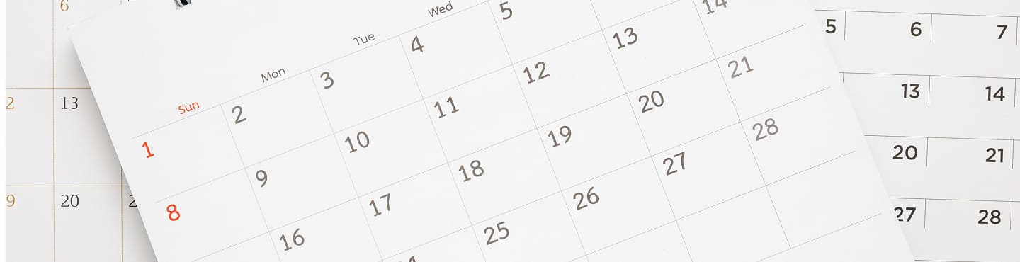 A close-up of two overlapping monthly calendars, with blog notes and numbers representing dates clearly visible. The calendars are laid out on a flat surface, showing weeks starting from Sunday.