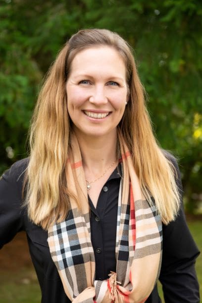 anna cummins, blonde woman with checkered scarf, smiling for the camera, waist up is visible