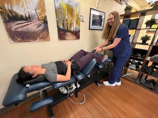 A woman lies on a medical table while a chiropractor adjusts her.